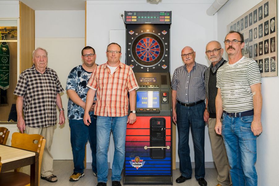 Mitglieder des Schützenvereins der Universitätskliniken Münster posieren im Vereinsheim vor einer Dartscheibe.