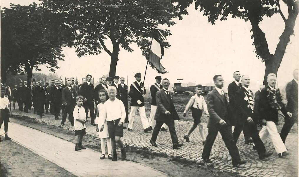 Rückmarsch nach dem Königsschießen in Münster: Männer in Schützenkleidung und Anzügen, mit Kindern auf einem gepflasterten Weg zwischen Bäumen.